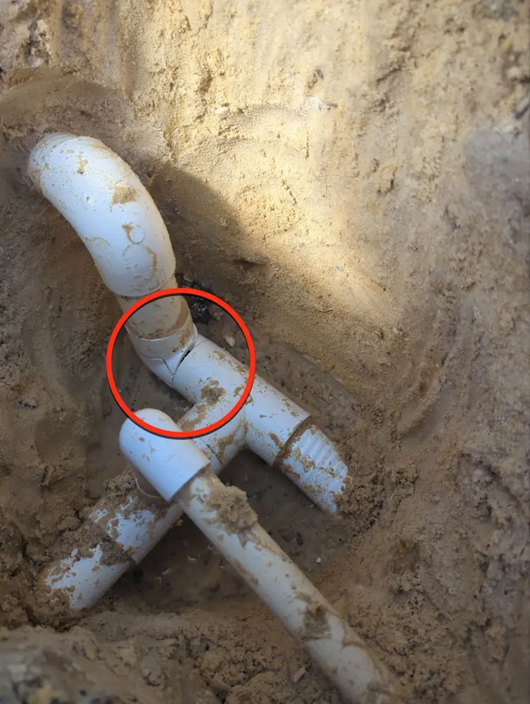 Broken underground pool pipe exposed in sand with the crack circled